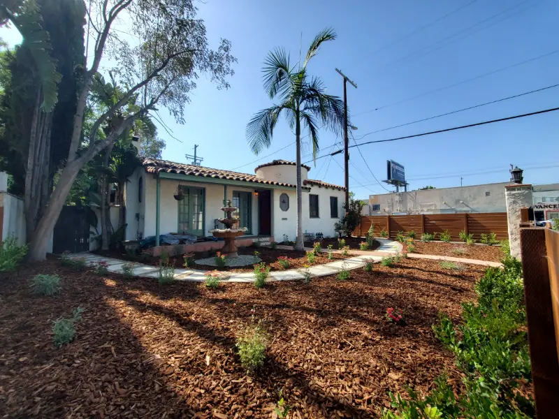 Newly planted native garden of gravel and young drought-tolerant shrubs in front of a white Spanish-style house