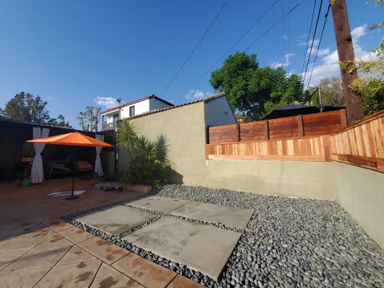 Backyard patio of concrete pavers and gravel enclosed by a new wood fence, with a shade umbrella