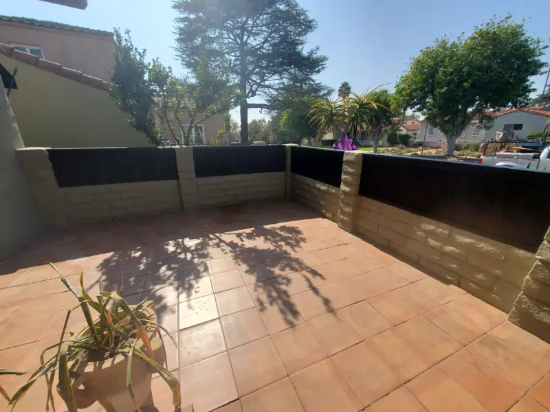 Walled backyard finished with a large tiled patio and a dark retaining wall
