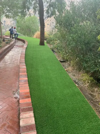 Narrow side yard finished with a strip of artificial turf beside a brick walkway